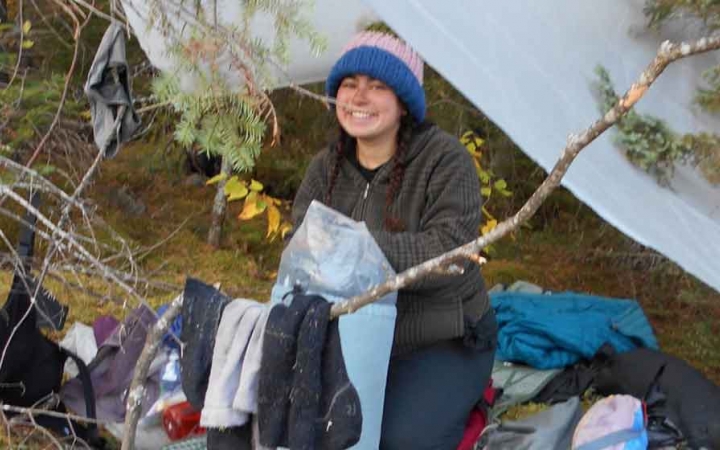 a student hangs clothes on a branch beside a tarp shelter on an outward bound course